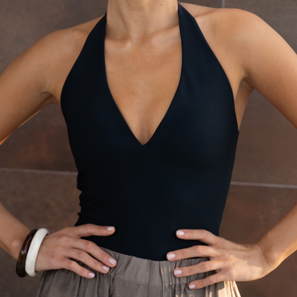 Black halter top with deep V-neckline on model wearing gray pants.